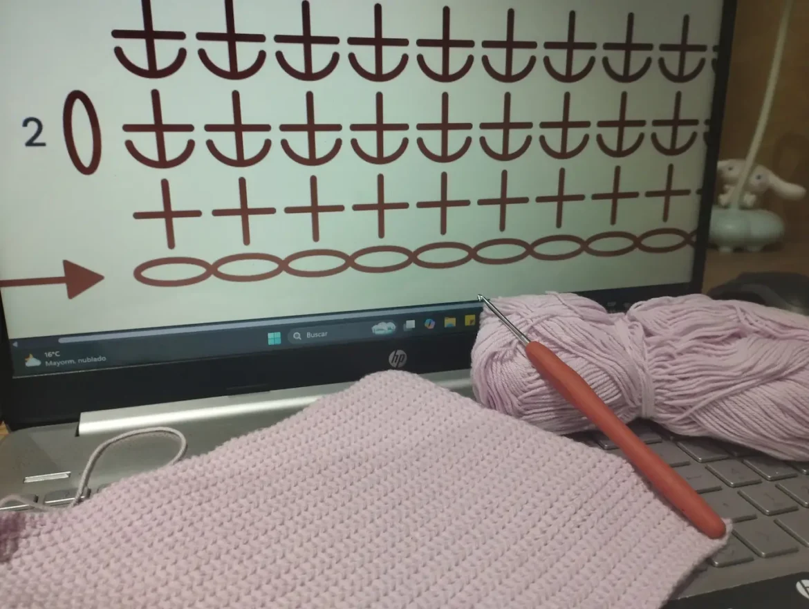 Gráfico del punto bajo en la hebra delantera a crochet en la pantalla de un portátil. Sobre el teclado hay un tejido en esta puntada de color lila, un ovillo del mismo color y una aguja de crochet
